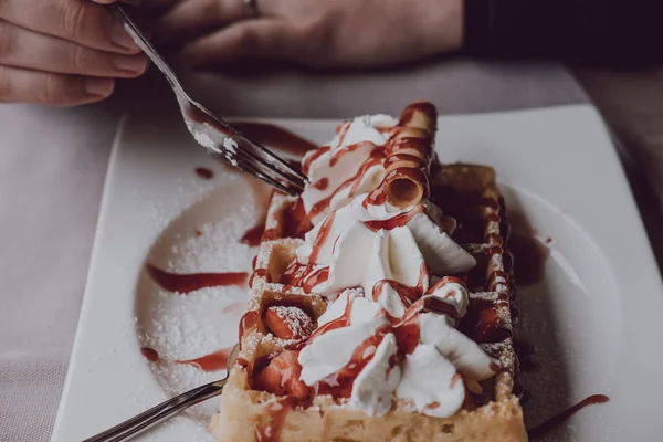 Manos masculinas sosteniendo un tenedor sobre el gofre con crema fresca y salsa Imágenes De Stock Sin Royalties Gratis