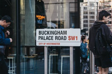 Buckingham Palace Road üzerinde sokak adı tabelası geçen insanlar, 