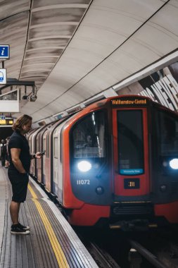 Adam bir Londra Metro İstasyonu platformunda onun kullanarak ayakta 