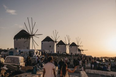 İnsanlar Mykonos Town 'da gün batımını izlemek için yel değirmenlerinin yakınında toplanıyor.,