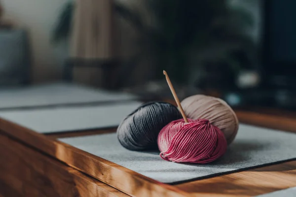 Tahta bir masaya ahşap kancalı üç farklı renkli yün yumağı. Pencereden gelen güneş ışığı üzerine düşüyor..