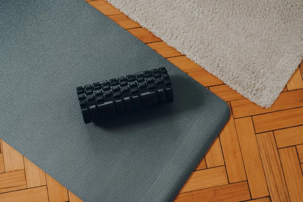 Eski parke zemin üzerinde siyah köpük rulo ve bir fitness paspas üst aşağı görünüm, seçici odak.