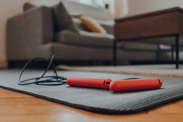 Close up of a jump rope on top of a fitness mat on a living room floor, interior of a modern flat, selective focus.