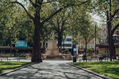 Londra, İngiltere - 13 Haziran 2020: Londra 'nın en popüler ve tipik olarak çok yoğun turistik bölgelerinden biri olan Leicester Meydanı' ndaki bir çeşmenin önündeki banklarda dinlenen çok az sayıda insan.