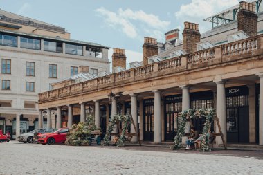Londra, İngiltere - 13 Haziran 2020: Covent Garden Market 'te çiçek desenli banklarda dinlenen çok az insan, genellikle güneşli bir yaz gününde Londra, İngiltere' nin en popüler turizm merkezlerinden biridir..