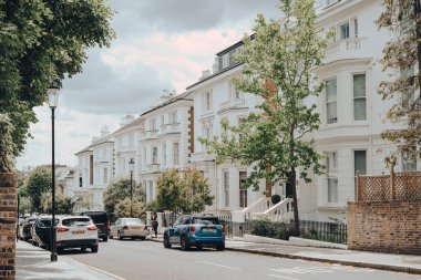 Londra, İngiltere - 20 Haziran 2020: Batı Londra 'da ünlülerin tercih ettiği zengin bir bölge olan Holland Park' taki beyaz Viktorya dönemi evlerinin önüne park edilmiş arabalar.