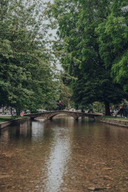 Bourton-on-the-Water, İngiltere - 12 Temmuz 2020: İngiltere 'nin Cotswolds kırsalındaki ünlü bir köy olan Bourton-on-the-Water' daki Windrush Nehri üzerinde küçük bir taş köprü üzerinde yürüyen kadın.