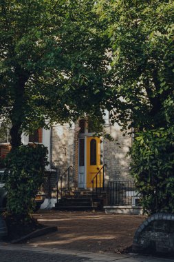 Londra, İngiltere - 20 Ağustos 2020: Crouch End 'de geleneksel olarak yaratıcı ve ailelerin tercih ettiği Crouch End' deki geleneksel bir teraslı evin parlak sarı ön kapısı, ağaçların arasından bakıyor..