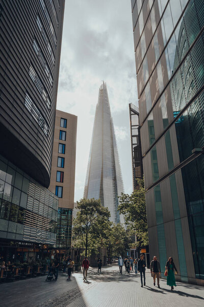 London, UK - August 25, 2020: View of The Shard between the buildings on More London, people walking in front. The Shard is are one of the most popular landmarks in London.