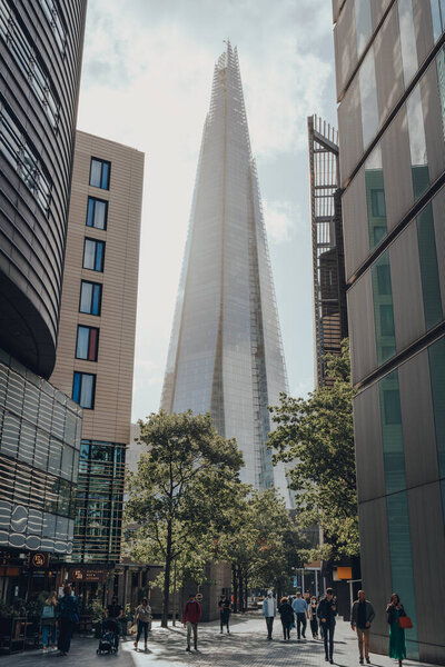 London, UK - August 25, 2020: View of The Shard between the buildings on More London, people walking in front. The Shard is are one of the most popular landmarks in London.