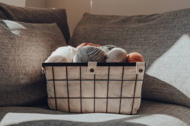 Bir sepet toprak renkli iplik, kanepenin üzerinde güneş ışığı, seçici bir odak..