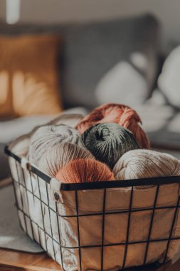 Toprak renkli iplikler bir sepetin içinde bir evin içindeki bir masada, penceresinden gelen güneş ışığı, seçici bir odak..