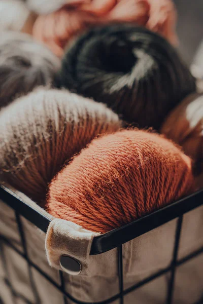 Close up of earth coloured merino wool yarn inside a basket, sunlight from the window on it, selective focus on the closest ball.