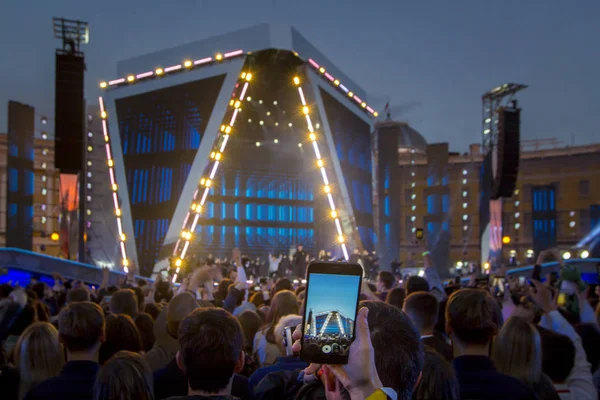 San Petersburgo, Rusia - 24 de junio de 2018: Mano con vídeo / foto de grabación de teléfonos inteligentes en el concierto de música en vivo, siluetas de multitud frente a luces de escenario brillantes . — Foto de Stock