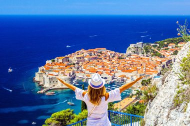 Happy young girl enjoys view of old town (medieval Ragusa) and Dalmatian Coast of Adriatic Sea in Dubrovnik. Blue sea with white yachts, beautiful landscape, aerial view, Dubrovnik, Croatia clipart