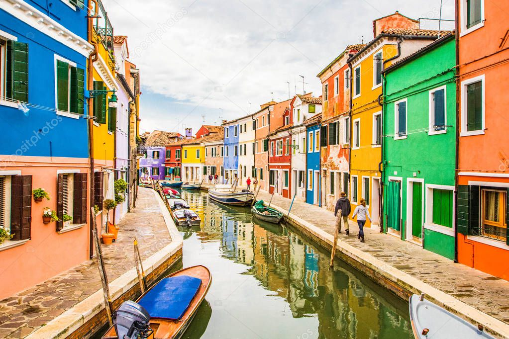 View on typical street scene showing brightly painted houses and boats with reflection along canal at Islands of Burano in Venice, Italy