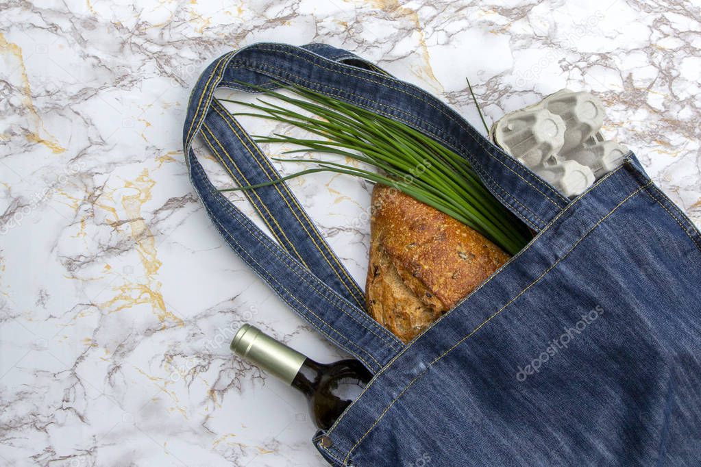 Fresh produce in blue denim market bag on marble kitchen table background, flat lay. Eco friendly reusable shopping bag for minimize waste, Earth Day, no plastic.