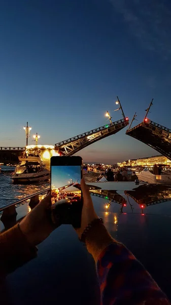 Girl takes photo on phone breeding Palace Bridge in St. Petersburg during White Nights. View from Neva River to raised bridge. Saint Petersburg, Russia