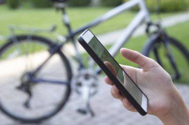 Akıllı telefon elinde kadın ve yeşil bokeh arka plan üzerinde bulanık bisiklet. Mobil iletişim ağı, bilgi seyahat konsepti veya bisiklet kiralama