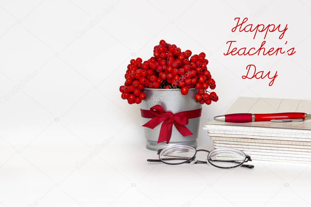 Happy Teacher's day greeting card - bouquet of red mountain ash in flower pot with satin ribbon, pile of notebooks, glasses and pen on white background. International school Teacher Day.