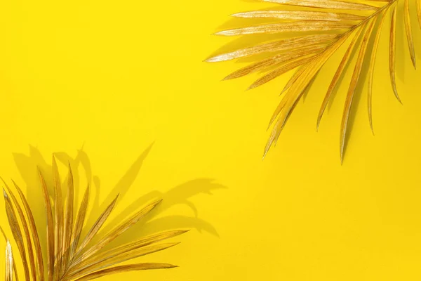 Golden palm leaves on yellow background. Creative minimal modern concept of organic beauty trend.