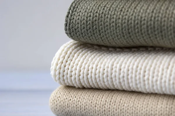 Pile of knitted cashmere sweaters on light blue wooden background. Folded autumn and winter clothing.