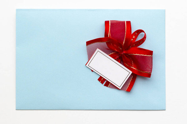 Blank paper blue envelope with red ribbon bow, letter for mail on white background, flat lay, top view. Concept postal service or greeting card