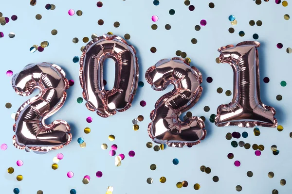 Gold pink balloons in form of numbers 2021 whis colorful shiny confetti on blue background. Happy New Year celebration. Flat lay, top view