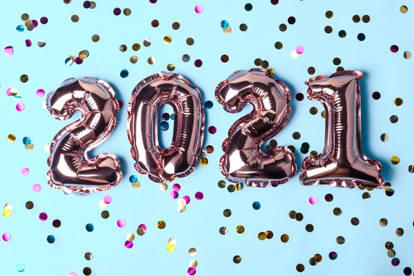 Gold pink balloons in form of numbers 2021 whis colorful shiny confetti on blue background. Happy New Year celebration. Flat lay, top view