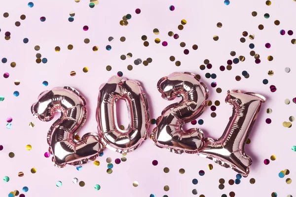 Gold pink balloons in form of numbers 2021 with colorful shiny confetti on pink background. Happy New Year celebration. Flat lay, top view