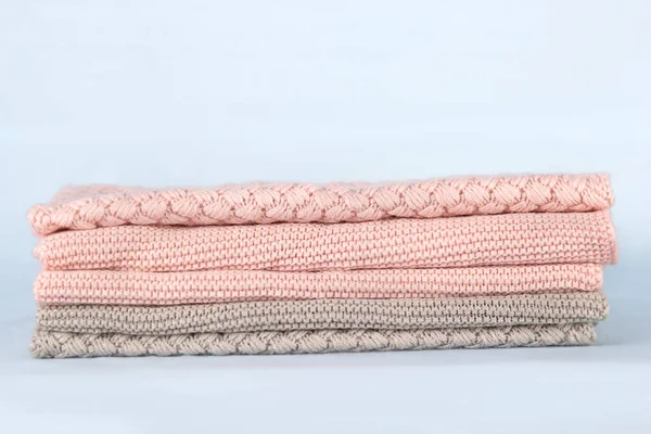 Pile of pink knitted cashmere scarves, sweaters on light blue background. Folded autumn and winter clothing.
