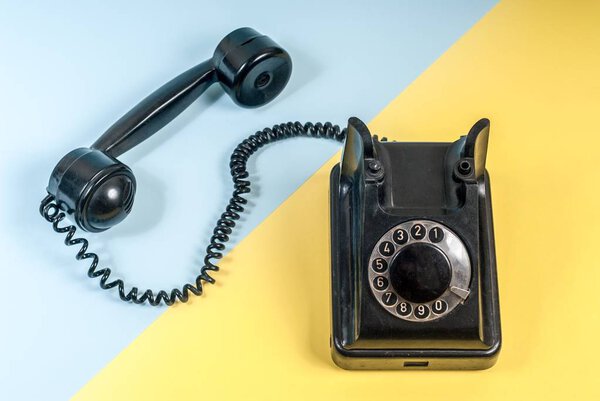 Винтажный черный телефон с гарнитурой и спиральным кабелем на синем и желтом
