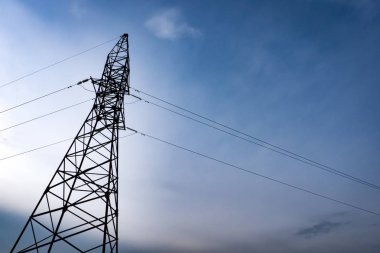 Elektrik akşam günbatımında deftere nakleder. Elektrik direkleri ve mavi gökyüzü.