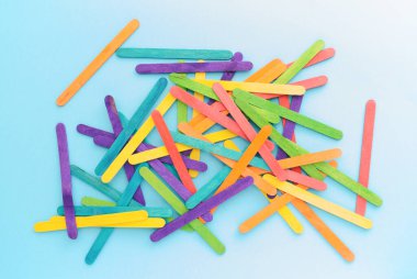 Sanat şekilleri ve nesneler yaratmak için kullanılan renkli tahta çubuklar. Mavi arkaplanda gökkuşağı rengi yapışıyor.