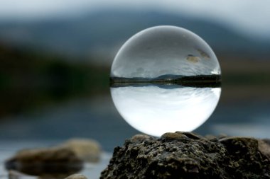 Suyun kıyısındaki bir gölde şeffaf bir lens topu. Lens topundan Lakeshore görüntüsü.