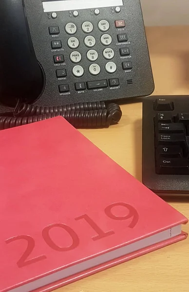 A workplace at an office with a pink calendar a phone and also a key board