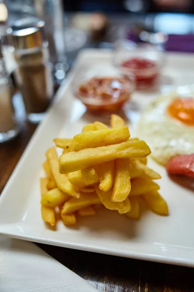 Meal closeup photo - french fries, fried eggs with ketchup. Blurred table setting background - image