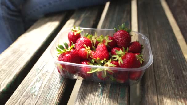 Main de femme caucasienne prend une fraise d'une boîte de fruits frais mûrs . — Video