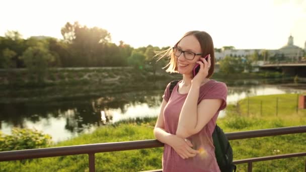 Ragazza in occhiali che parla al telefono su un ponte della città al tramonto . — Video Stock
