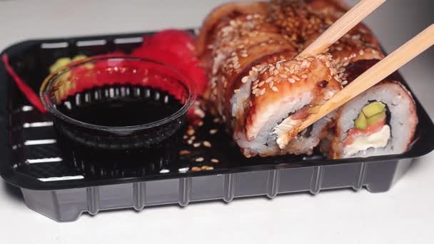 Mano con palillos tomando sushi. Rollos de sushi en un recipiente de plástico oscuro. Movimiento lento . — Vídeos de Stock