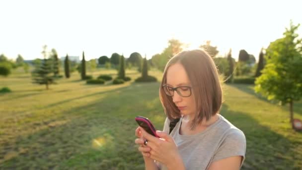 Mooi aantrekkelijk meisje chatten op haar smartphone met vriend. Haren wapperen in de wind van de zomer. — Stockvideo