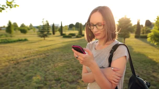 Fille décontractée dans des lunettes bavardage utilise smartphone. Le soleil du soir brille .