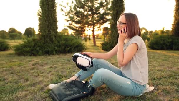 Girl in glasses talking on smartphone and holding a virtual reality glasses. — Stock Video