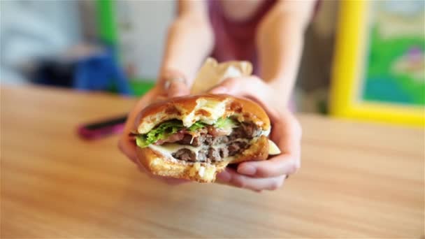 Una gran hamburguesa en manos de una mujer. Fondo borroso . — Vídeos de Stock