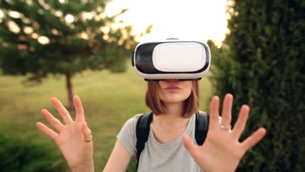 Menina alegre usa um óculos de realidade virtual no jardim. Luz do pôr do sol, hora de ouro . — Vídeo de Stock