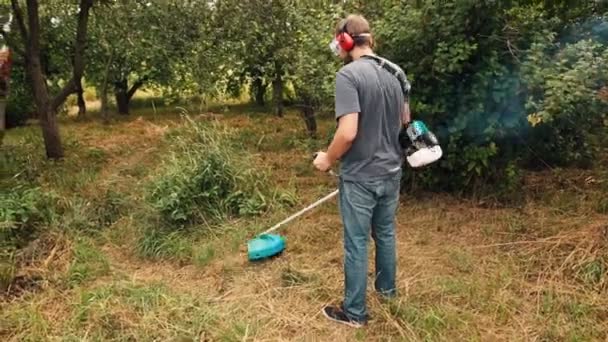 ひものトリマーを使用して果樹園の緑の草の切断の芝刈機. — ストック動画