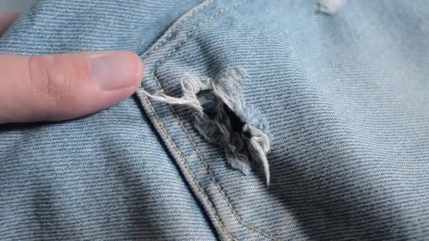 Mão tocando jeans esfarrapados. O buraco na calça azul com fugas . — Vídeo de Stock
