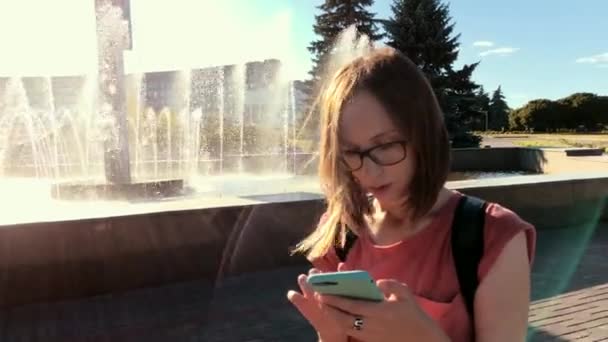 Kvinna står vid fontänen och använda sin smartphone utomhus. — Stockvideo