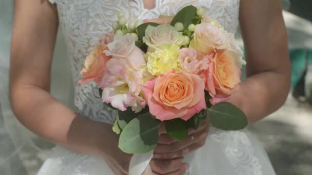 Bouquet de mariage entre les mains de la mariée. Journée ensoleillée, roses colorées, gros plan . — Video