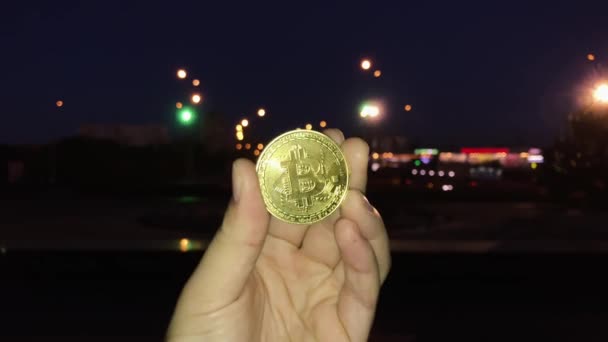 Mannelijke hand met bitcoin gouden medaille op de achtergrond van de nacht-stad. — Stockvideo